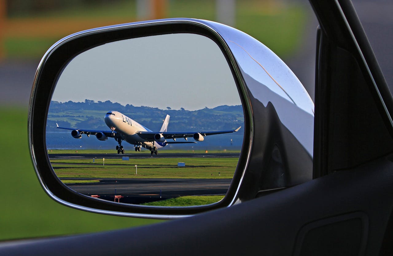 A jet airplane taking off is reflected in a car