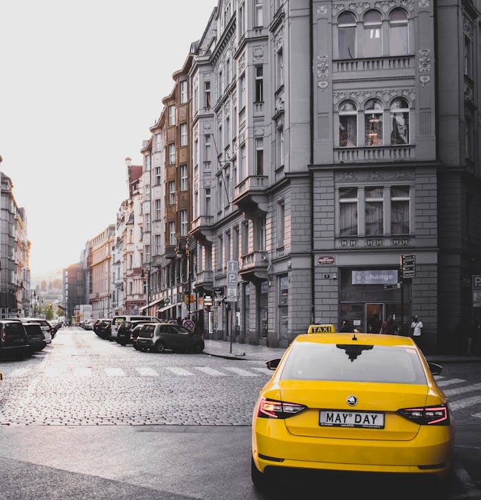 Yellow taxi in a classic Prague street with historical architecture under daylight.